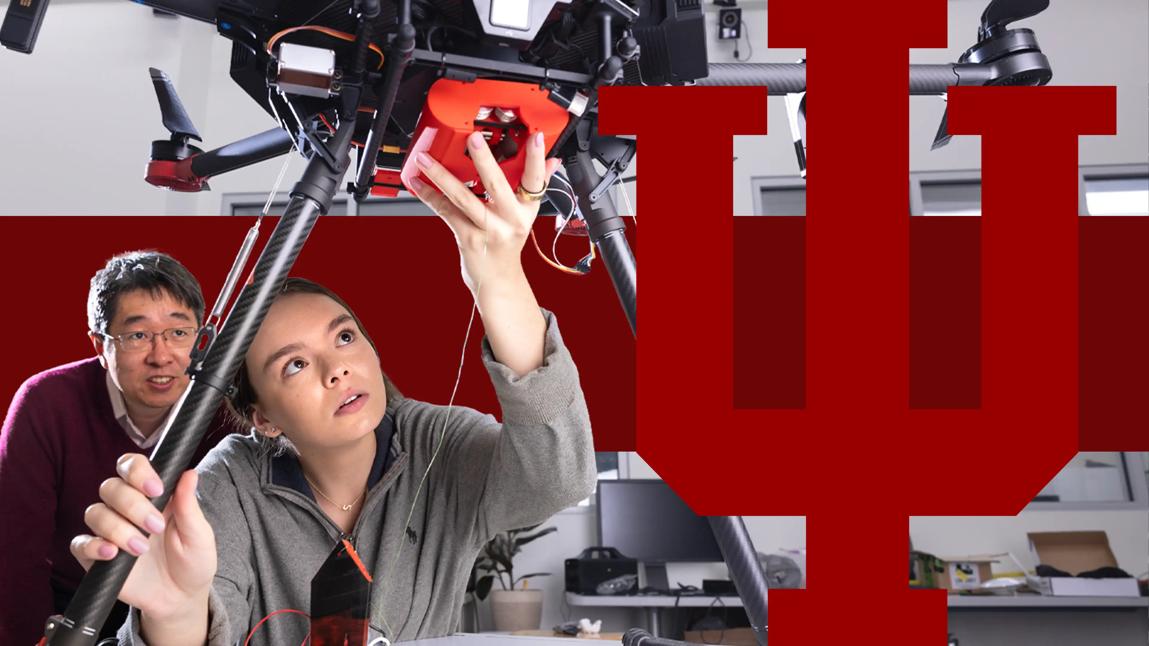 A female student looks up in wonder while working under a large drone, with a male professor watching her intently.