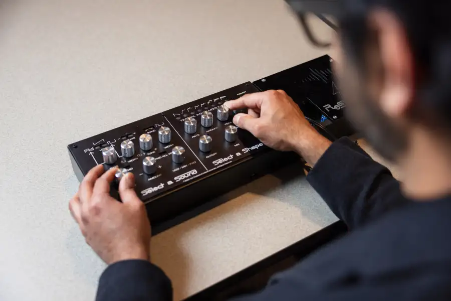 An over-the-shoulder view of a man manipulating a vintage synthesizer’s buttons.